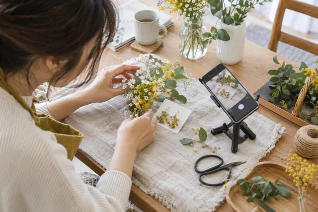 花や小物を整え、スマートフォンで投稿用の写真を撮る手元
